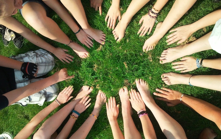 Ungdomar i ring på gräsmatta som visar händer och fötter med grönmålade naglar. Foto: Pixabay