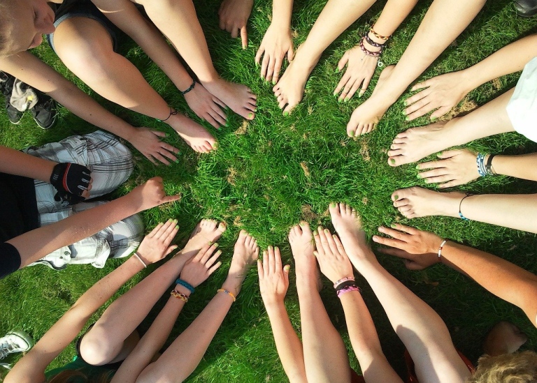 Ungdomar i ring på gräsmatta som visar händer och fötter med grönmålade naglar. Foto: Pixabay