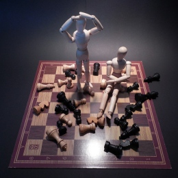 Chessboard with scattered pieces and two wooden dolls. Photo: Succo from Pixabay.