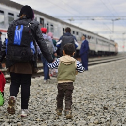 Liten pojke går vid ett tåg och håller sin mamma i handen. Migranter.